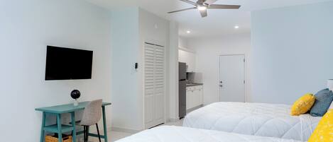 A bedroom with two beds, a desk, a chair, a TV, and a ceiling fan.