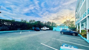Um estacionamento com um edifício ao fundo, um carro coberto e um céu limpo.