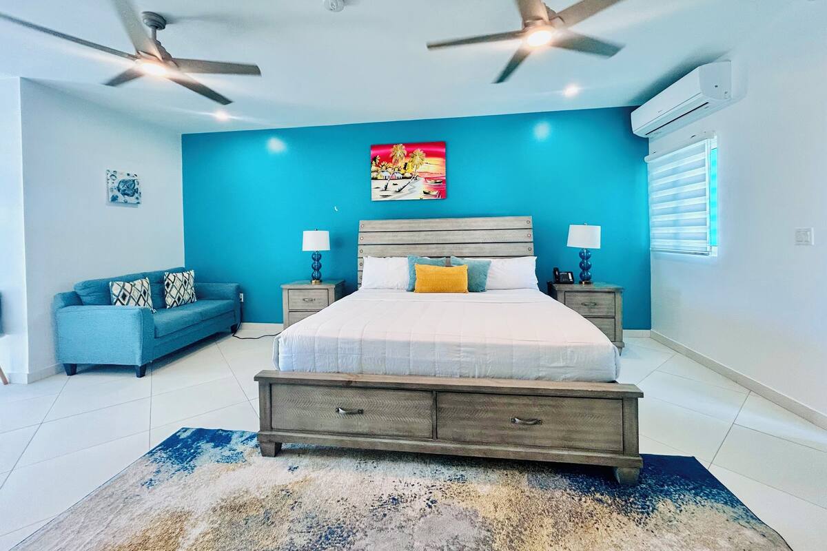 Une chambre à coucher avec un lit, deux tables de chevet, un canapé bleu et un ventilateur de plafond.
