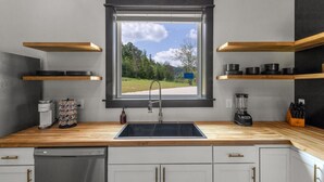 Una cocina moderna con vistas por la ventana, estantes de madera, una cafetera y una licuadora.