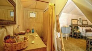 Quarto com tenda, banheiro, cama e uma pequena mesa com abajur.