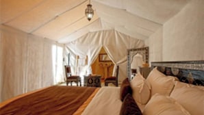 Um quarto tipo tenda com uma cama grande, uma mesa pequena e uma cadeira.