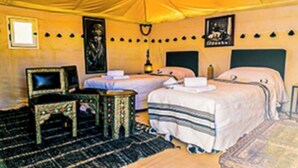 Quarto com tenda, duas camas, uma mesinha e uma cadeira.