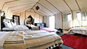 Um quarto tipo tenda com duas camas, um tapete vermelho e um candeeiro pendente.