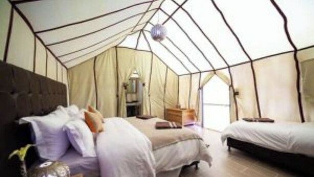Um quarto em estilo tenda com duas camas, uma mesinha de cabeceira e um candeeiro suspenso.