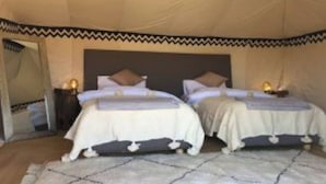 Habitación con carpa, con dos camas, cada una con almohada y manta. Hay mesitas de noche con lámparas.