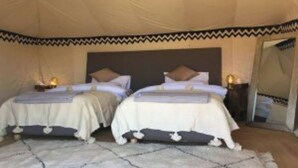 Una habitación con tiendas de campaña, dos camas, cada una con una almohada y una mesita con lámpara.