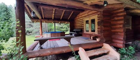 A rustic wooden cabin with a covered patio area, a pool table, and a seating area with a table and chairs.