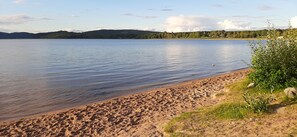 A sandy beach with calm water, a clear sky, and distant hills.