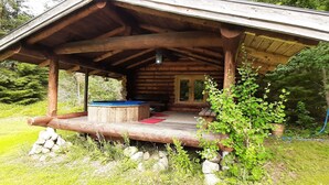 Eine rustikale Holzhütte mit einer Veranda, einem Whirlpool und einem Kamin aus Stein.