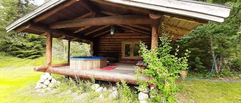 Een rustieke houten chalet met een overdekte veranda, een bubbelbad en een stenen open haard.