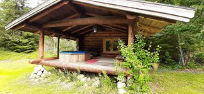 Una cabaña de madera rústica con un porche cubierto, un jacuzzi y una chimenea de piedra.