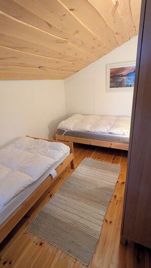 A small, cozy room with two wooden bunk beds, a wooden ceiling, and a framed picture on the wall.