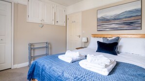 Een netjes opgemaakt slaapkamer met een bed, een schilderij en een witte deur.