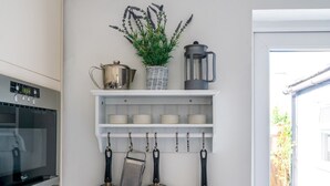 Een keuken met een witte plank waarop keukengerei, een koffiezetapparaat en een potplant staan.