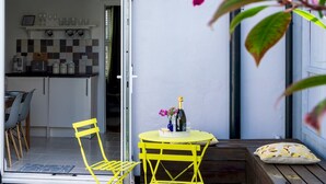 Een moderne keuken met een betegelde achterwand, een eethoek met gele stoelen, en een kleine tafel met een fles en bloemen.
