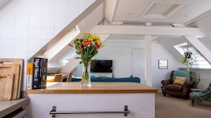 Un loft moderne avec un plafond en pente, une table à manger en bois, un vase rempli de fleurs, une bibliothèque, un fauteuil en cuir marron et un téléviseur.