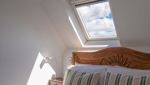 Une chambre avec un puits de lumière, une tête de lit en bois et des coussins à rayures.