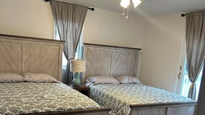 A bedroom with two beds, wooden headboards, a nightstand with a lamp, and a ceiling fan. - Fully renovated modern beach home in Orltey Beach
 (Seaside Heights)