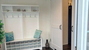 A room with a wooden floor, a bench with storage drawers, a sliding door, and a white wall with hooks. - Fully renovated modern beach home in Orltey Beach
 (Seaside Heights)