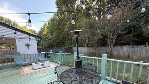 Eine Terrasse im Freien mit Metallstühlen und einem Tisch, umgeben von einem Holzzaun und Bäumen.