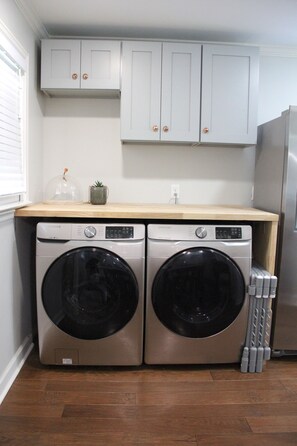 A laundry area with two front-loading washing machines, a small potted plant, and a stainless steel refrigerator.