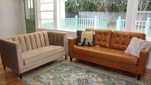 Ein Zimmer mit einem beigefarbenen Sofa, einem braunen Ledersofa und einem Teppich mit Muster.