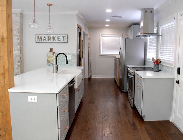 A kitchen with a white countertop, stainless steel appliances, and a wooden floor.
