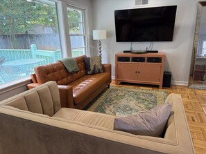 A living room with a brown leather sofa, a beige sofa, a wooden cabinet, a television, and a large window.