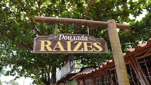 A wooden sign with the text "Pousada RAIZES" hanging from a wooden beam. - Pousada Raízes (Alto Paraíso de Goiás)