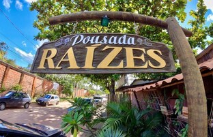 Un letrero de madera con el nombre 'Pousada Raizes' en letras doradas.