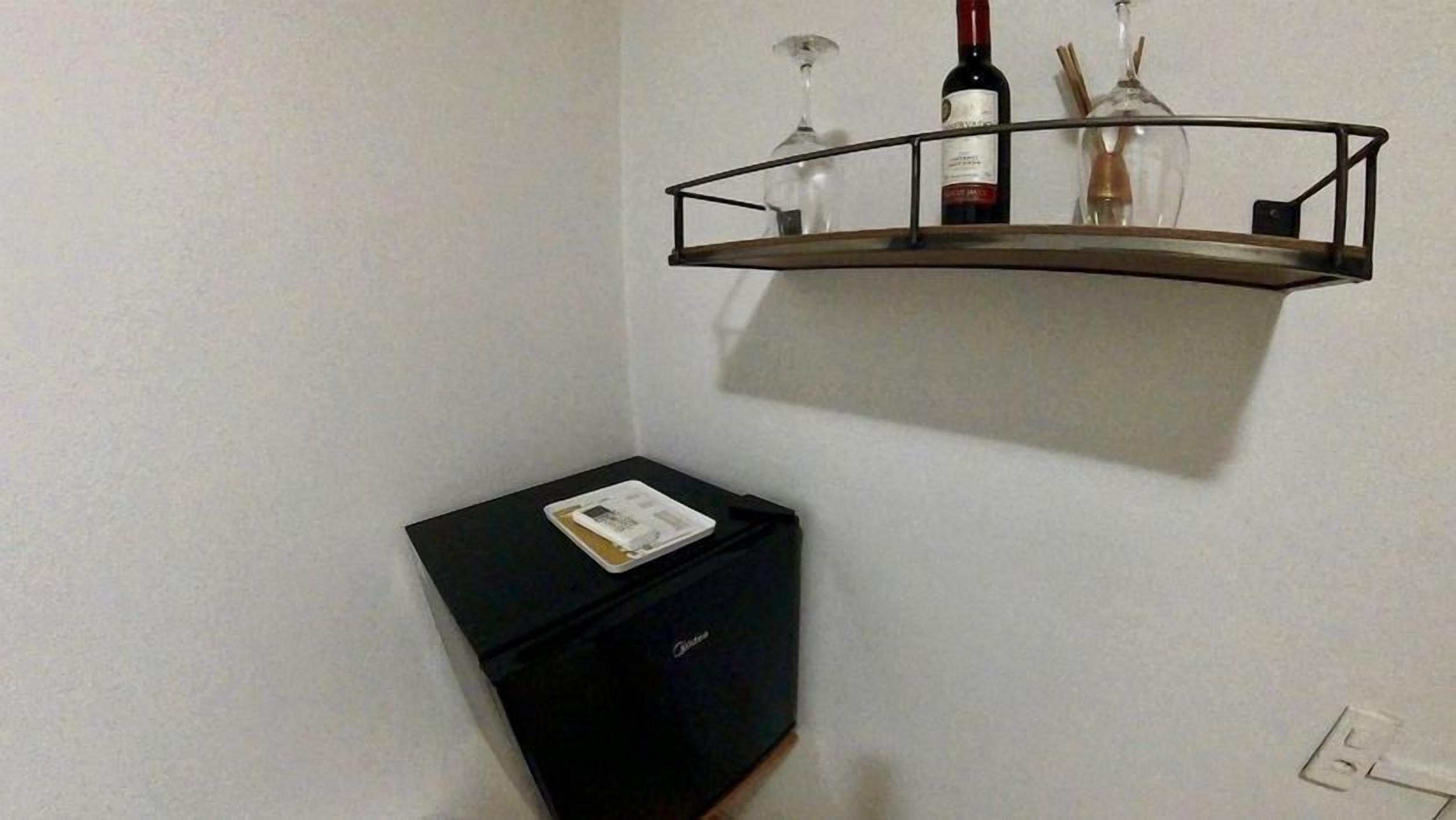 A small room with a black cabinet, a wine rack with bottles and glasses, and a power outlet on the wall.