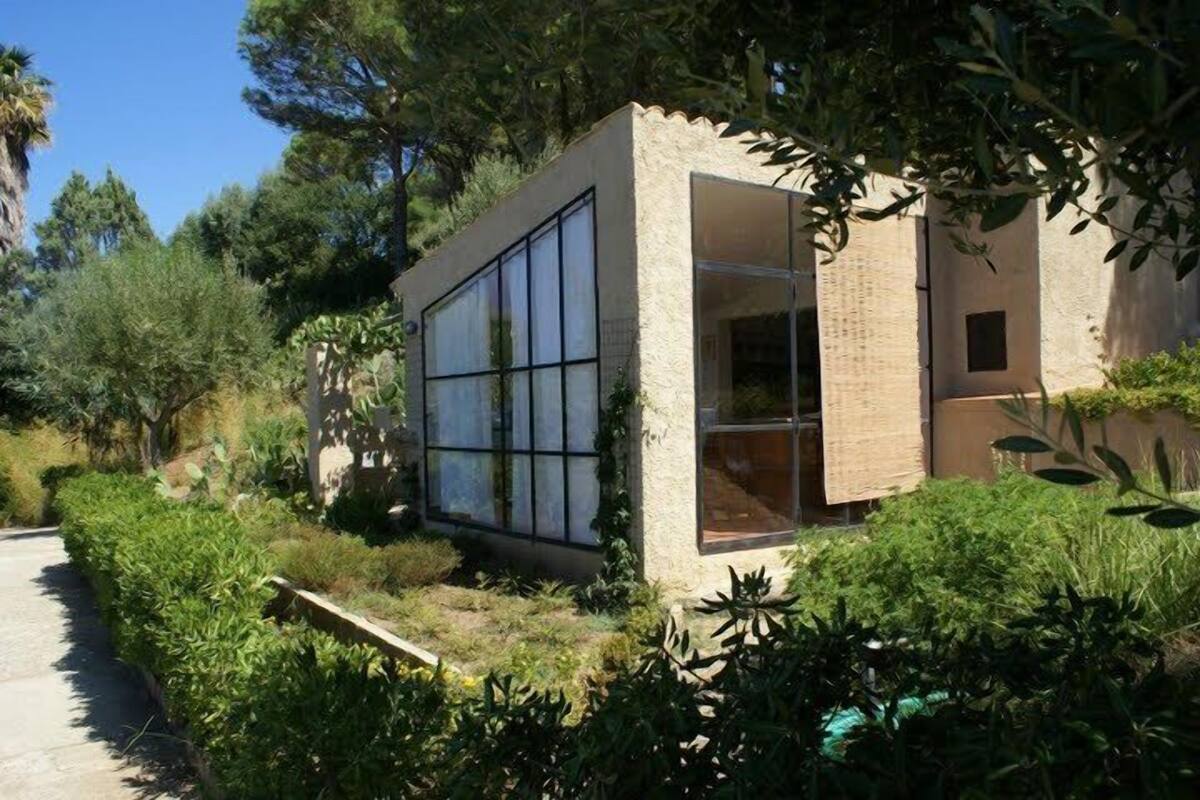 A modern building with large windows and a brick exterior, surrounded by lush greenery.