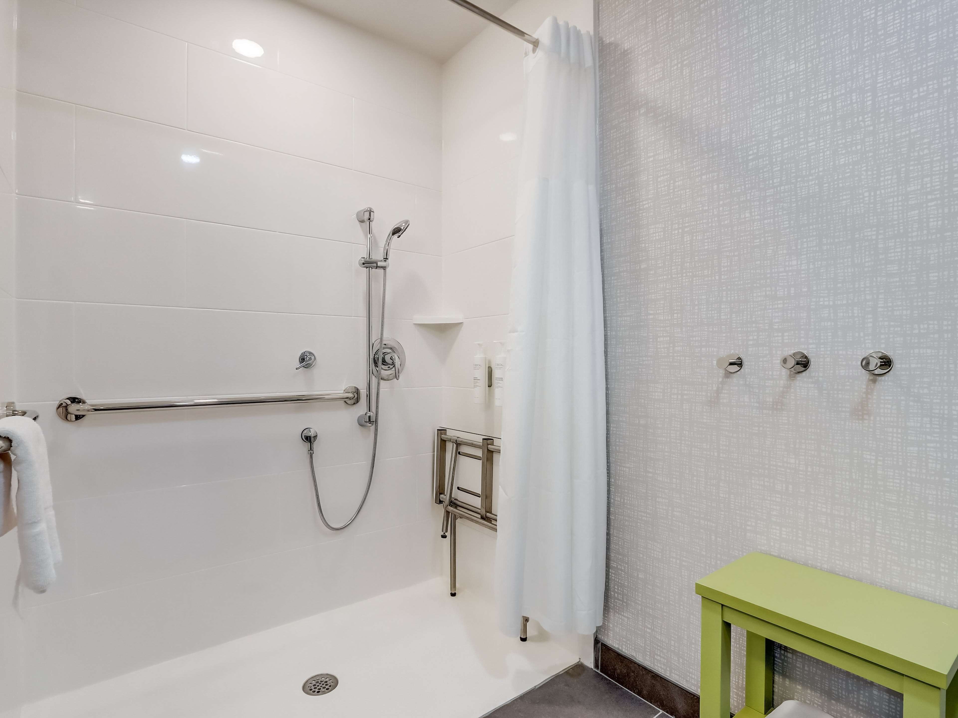 Un baño moderno con cabina de ducha, barras de apoyo, un mueble de tocador verde y un perchero para toallas.