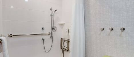 Un baño moderno con cabina de ducha, barras de apoyo, un mueble de tocador verde y un perchero para toallas.