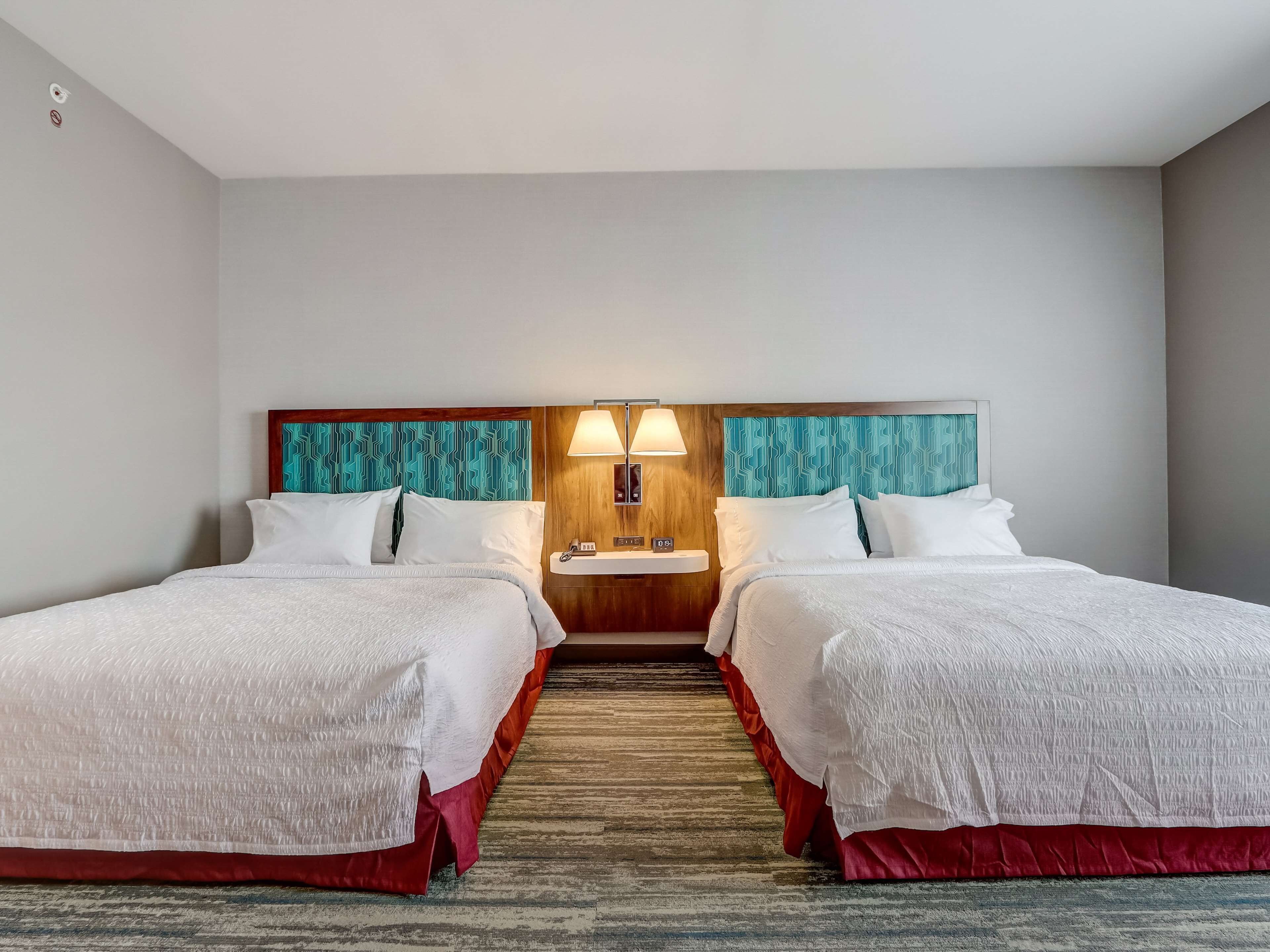 Een hotelkamer met twee bedden, een houten hoofdbord, een nachtkastje met een lamp en een klein wastafeltje.