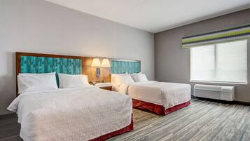 A hotel room with two beds, a large window, a wall-mounted air conditioner, and a headboard with a geometric pattern.