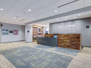 A reception area with a wooden reception desk, a 'Welcome to the Buck Eye State' sign, a snack shop, and a 'Make Everyone Happy' mat. - Hampton Inn & Suites Cincinnati Midtown Rookwood (Cincinnati)