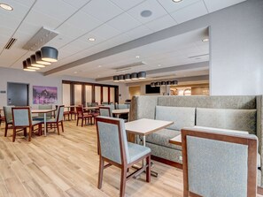 A modern dining area with wooden tables and chairs, a seating area with cushioned benches, and a wall-mounted TV. - Hampton Inn & Suites Cincinnati Midtown Rookwood (Cincinnati)