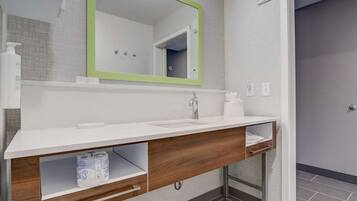 A modern bathroom with a white vanity, a green-framed mirror, a towel rack, and a toilet paper dispenser.