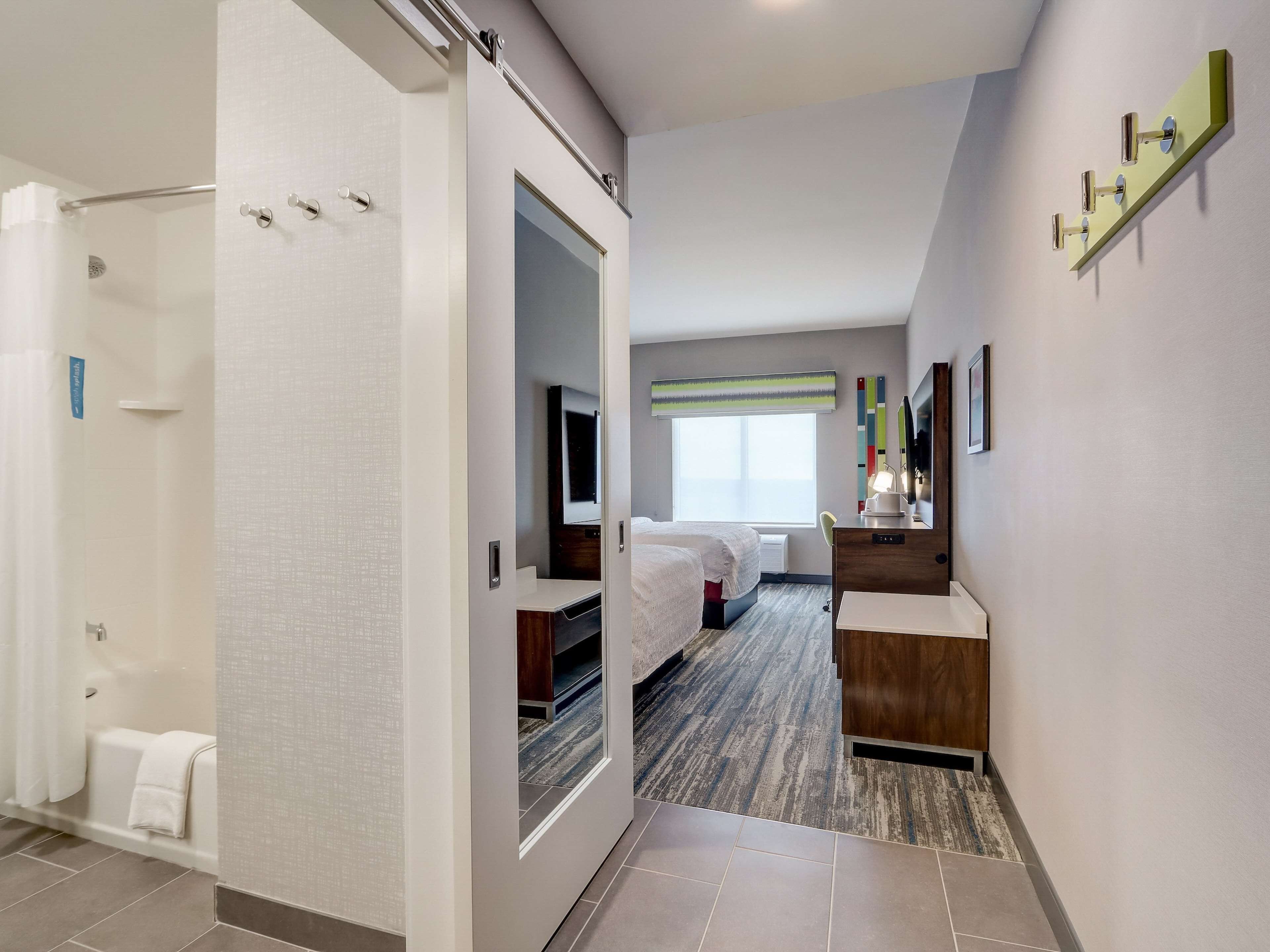 A hotel room with a shower, a bed, a desk, and a window.