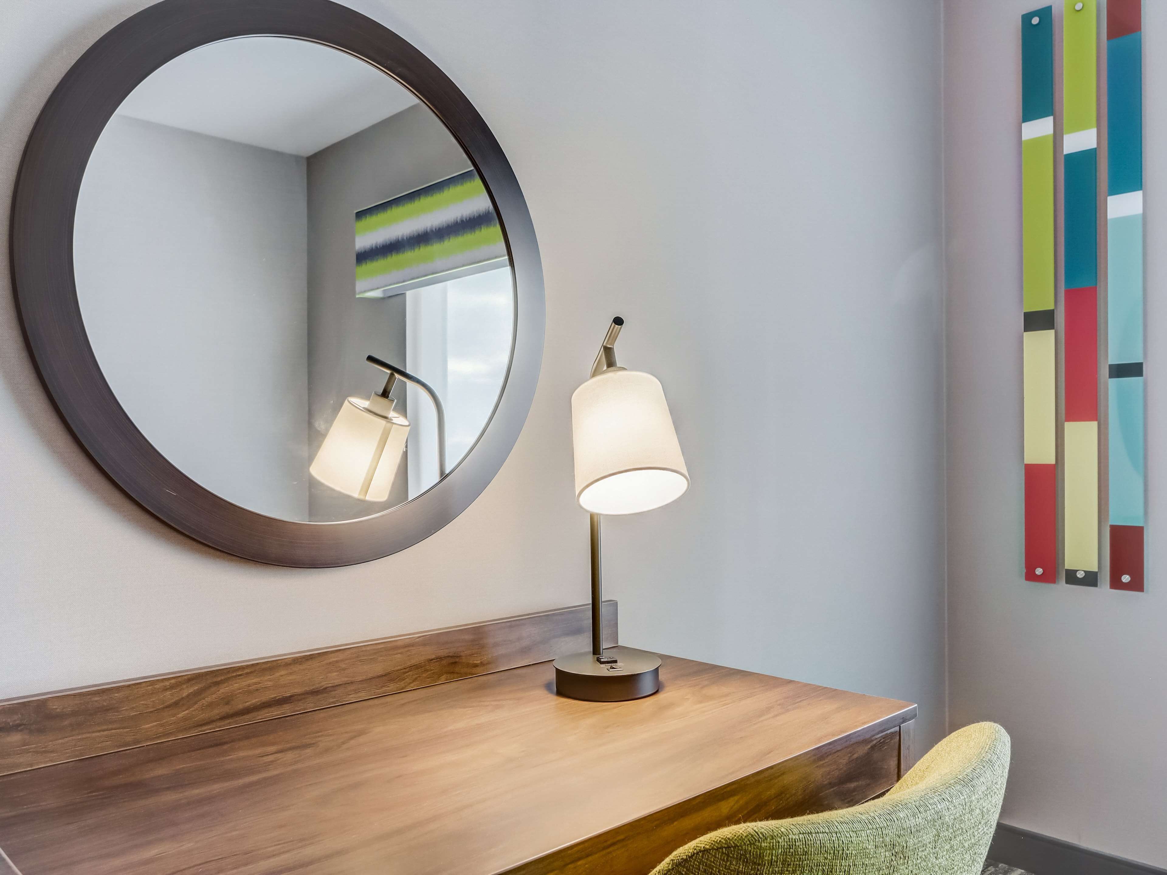 A round mirror with a dark frame, a modern desk lamp, and a chair.
