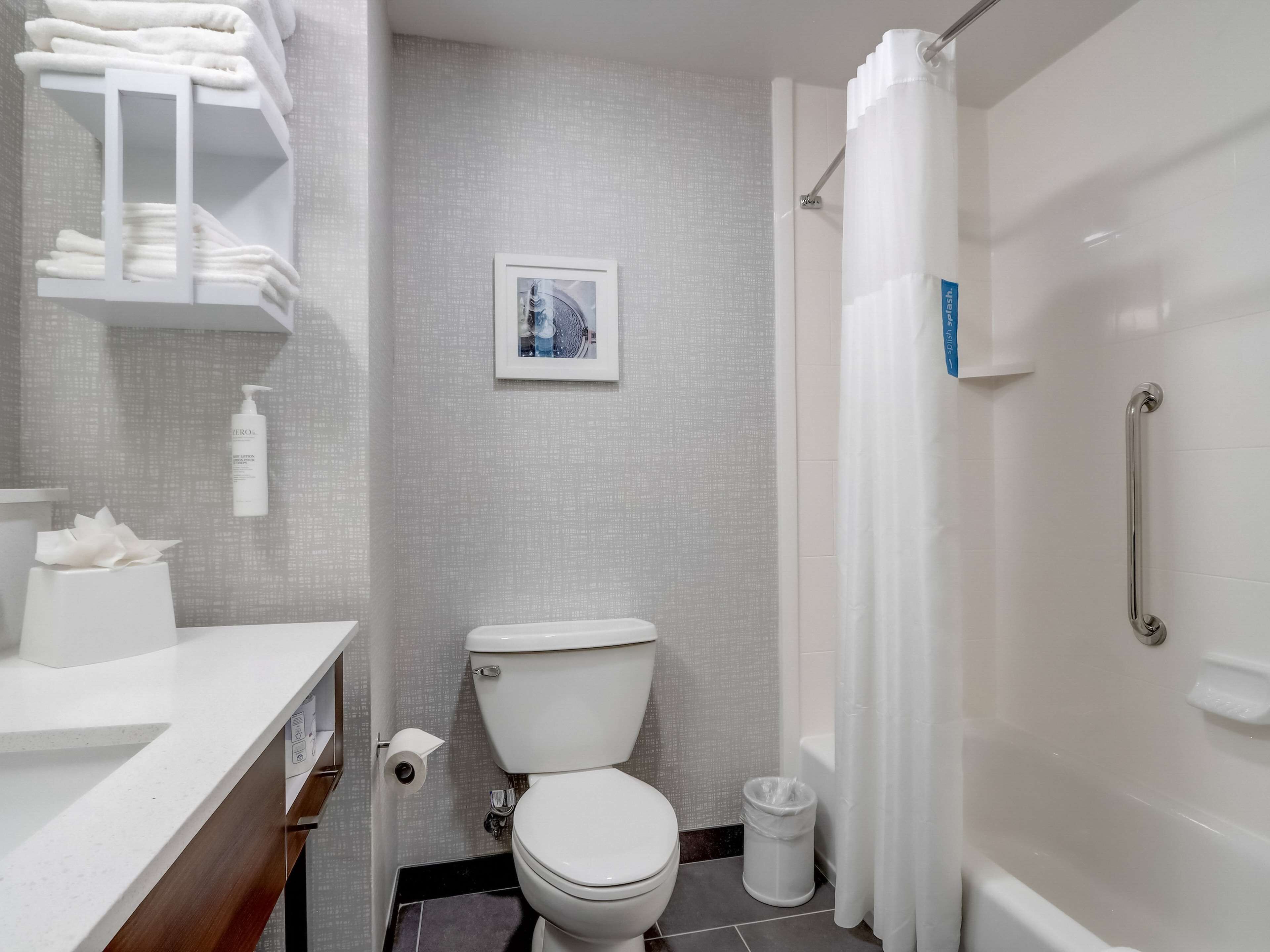 Un baño moderno con inodoro, ducha con cortina, lavamanos y toallero, y un cuadro en la pared.