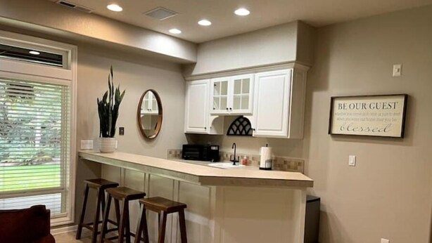 A kitchen with a central island, bar stools, white cabinets, and a 'BE OUR GUEST' sign. - The Cellar @Lively Farm
a Family Friendly Hobby Farm Stay (Newberg)