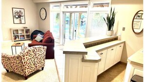 A modern kitchen with white cabinetry, a built-in island, and a dining area with a red sofa and patterned armchair. - The Cellar @Lively Farm
a Family Friendly Hobby Farm Stay (Newberg)