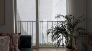 A room with a sliding glass door leading to a balcony, a potted plant, and a chair with a throw blanket. - Romantic Gem in Santa Catarina (Lisboa)