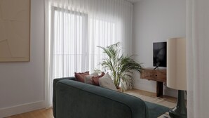 A modern living room with a green sofa, a potted plant, a flat-screen TV, and a lamp. - Romantic Gem in Santa Catarina (Lisboa)