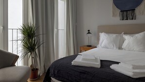 A hotel room with a bed, a nightstand, a lamp, a potted plant, and a view of the outdoors. - Romantic Gem in Santa Catarina (Lisboa)