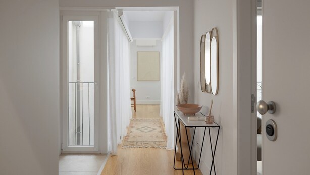 A hallway with a wooden floor, a white door on the right, and a view into another room with a chair and a table. - Romantic Gem in Santa Catarina (Lisboa)
