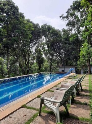 Relax by the serene pool surrounded by lush greenery and lounge chairs.